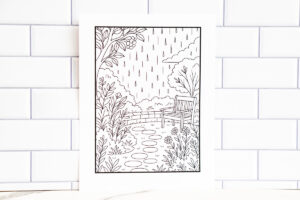 Close-up of a garden-themed relaxation coloring page with raindrops, plants, and a bench, propped up in front of a white tile wall.