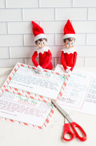 Two Elf on the Shelf dolls sit behind a set of printed &ldquo;Sorry I&rsquo;m Late&rdquo; telegrams and a customizable North Pole letter, with red scissors resting nearby.
