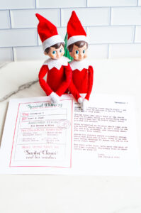 Two Elf on the Shelf dolls sit behind a printed sorry I'm late letter from the North Pole, with their hands resting on the page.