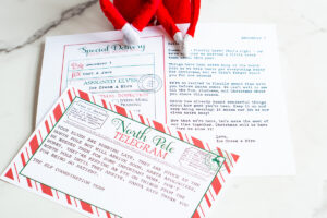 Two Elf on the Shelf dolls sit behind layered Christmas printables, including a &ldquo;Sorry I&rsquo;m Late&rdquo; North Pole telegram and explanation letter.