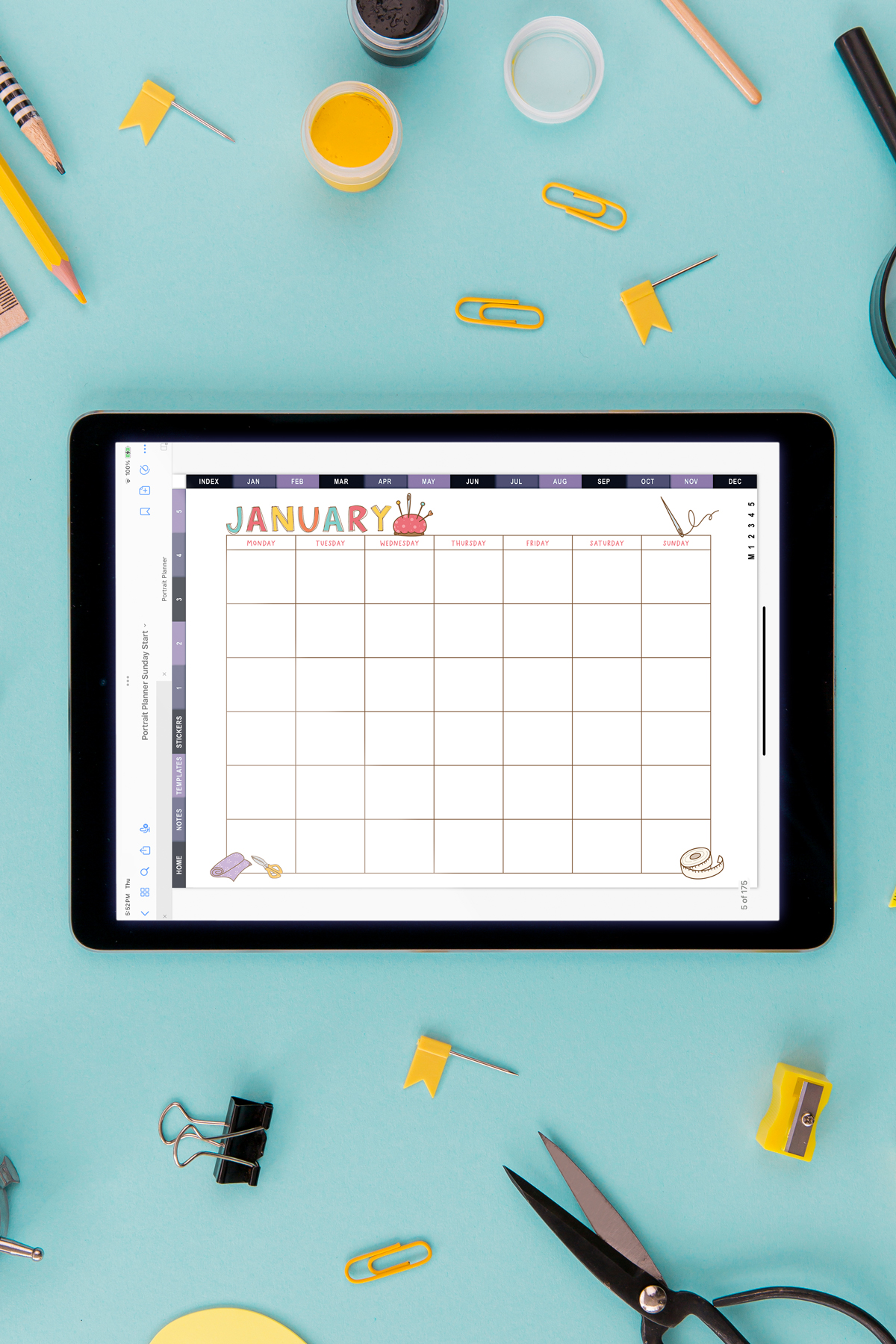 Digital tablet displaying the January craft-themed undated calendar on a teal background, surrounded by yellow stationery, paint jars, scissors, clips, and craft tools.