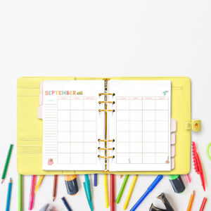 Open yellow planner showing the September craft-themed undated calendar, placed above scattered colored pencils, markers, and craft tools.