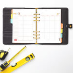 Open black planner showing the May craft-themed undated calendar, styled with a tape measure and yellow level positioned below.