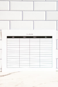 A portrait view of the lined contact list printable showing the full grid layout with a black header row. The page is set against a glossy white subway-tile wall.