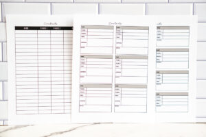 A photo of three printable contact list pages standing upright against a white subway-tile background. The left page features a black-topped column layout with rows for names, two phone numbers, and email. The middle and right pages show boxed contact-card layouts in muted colors with spaces for name, phone numbers, email, address, notes, and socials.