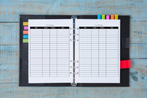 An open black planner sitting on a distressed blue wooden surface, holding two lined contact list pages with black headers. Colorful planner tabs are visible along the left and right edges.