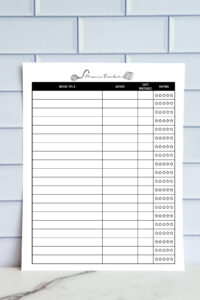 A black-and-white printable movie tracker sheet featuring list-style columns for movie title, genre, date watched, and star rating, shown in front of a light tile wall.
