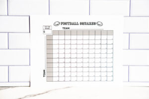 Printable football squares sheet displayed upright against a white subway-tile wall, showing a clean 100-square grid with spaces for teams, cost per square, and payout sections.