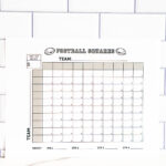 Football squares printable propped against a white subway-tile backsplash with the grid and team labels clearly visible.