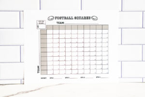 Football squares printable displayed on a white marble surface with a subway-tile backsplash, showing the full blank grid.