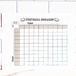 Football squares printable positioned on a marble countertop with a subway-tile wall behind it, showing the empty squares and team labels.