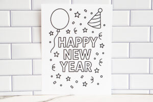 A simple &ldquo;Happy New Year&rdquo; coloring page displayed against a white subway-tile wall, featuring a large balloon, a striped party hat, and scattered stars and confetti.