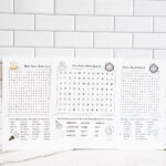 Alt text: Wide photo showing three New Year’s word search printables arranged in a row against a white subway tile backdrop, highlighting the different designs included in the set.