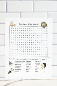 A medium-difficulty New Year&rsquo;s word search printable shown against a white subway tile background, featuring a larger puzzle grid and an expanded list of themed words decorated with festive illustrations.