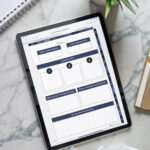 Flat-lay image of an iPad on a marble desk showing the Goal 1 page of the digital planner, surrounded by a coffee cup, notebook, pencil, and small potted plants.