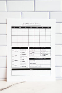 Printed monthly period tracker page displayed against a white subway tile background. The page features a blank monthly calendar grid, a symptom key including spotting, cramps, mood swings, and more, a section to rate the month&rsquo;s period (on time, early, late, normal, worse, better), a period stats table, and a large notes area at the bottom.