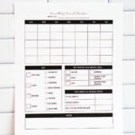 Printed monthly period tracker page shown upright in front of a white subway tile wall. The layout features an empty monthly calendar, symptom checkboxes, a section to mark period timing and quality, monthly stats, and a large notes section.