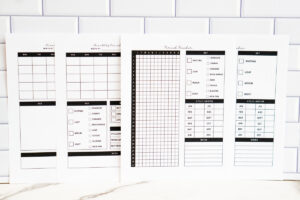 &ldquo;Four printable period tracker pages displayed side by side against a white subway tile background. The set includes two monthly trackers with blank calendars and symptom keys, and two yearly trackers with a 31-day grid, symptom checklists, cycle length charts, and notes sections.