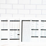 &ldquo;Four printable period tracker pages displayed side by side against a white subway tile background. The set includes two monthly trackers with blank calendars and symptom keys, and two yearly trackers with a 31-day grid, symptom checklists, cycle length charts, and notes sections.