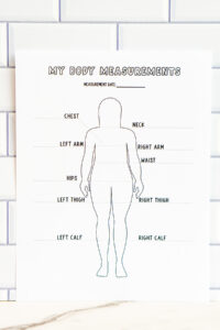 A printed &ldquo;My Body Measurements&rdquo; tracker with a full-body outline and labeled measurement areas displayed vertically against a white subway tile wall.
