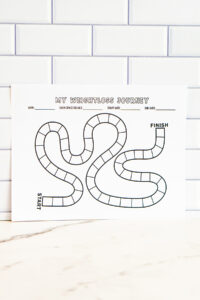 A printed version of the &ldquo;My Weightloss Journey&rdquo; game-board style tracker shown vertically against a white subway tile wall. The winding path of blank boxes leads from START at the bottom to FINISH at the top right.