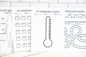 A lineup of multiple printed weight loss and measurement trackers standing side by side against a white subway tile wall, including the body outline measurement tracker, scale icon tracker, thermometer tracker, honeycomb tracker, and game-board-style tracker.