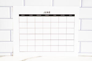 Horizontal undated June monthly calendar page with a simple black-and-white grid layout, shown against a bright white subway tile background.