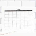 Minimalist undated June monthly calendar printed on white paper, displayed upright against a white subway tile backsplash with a marble countertop below.