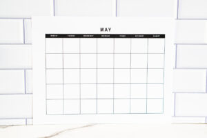Clean black-and-white undated May calendar page shown horizontally against a white subway tile wall, sitting on a marble surface.