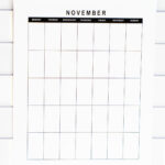 Undated November monthly calendar shown in a tall vertical layout against a white subway tile backsplash, photographed with a bright, clean aesthetic.