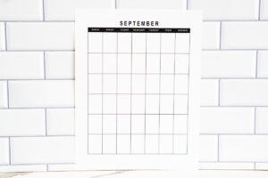 Vertical undated September monthly calendar page with a simple grid layout, standing against a white subway tile backsplash.