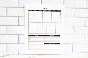 Undated July monthly calendar page featuring a full grid and lower sections for To Do, Important, and Monthly Focus, shown against a white subway tile backsplash.