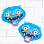 Two finished Valentine cards shaped like a blue cartoon blue Derpy from KPop Demon Hunters. They are placed on a white tile surface. Each demon has bright blue skin, pointed ears, glowing yellow-to-orange eyes, and a wide open mouth with sharp white teeth. A small Valentine card sticks out of each demon&rsquo;s mouth like a tongue, with one reading &ldquo;Happy Valentine&rsquo;s Day&rdquo; and the other reading &ldquo;Hello Friend."