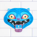 A single KPop Demon Hunters Inspired Valentine card shaped like a blue cartoon blue Derpy from KPop Demon Hunters. It is placed on a white tile surface.The Derpy looks like a blue tiger - has bright blue skin, pointed ears, glowing yellow-to-orange eyes, and a wide open mouth with sharp white teeth. A small Valentine card sticks out of its mouth like a tongue, with one reading &ldquo;Happy Valentine's Day."