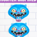 A tall vertical image shows a close-up of a single blue demon Valentine card centered on a white subway tile background. A purple banner across the top reads &ldquo;KPOP DEMON HUNTER INSPIRED.&rdquo; The Derpy&rsquo;s bright eyes, exaggerated smile, and fang-filled mouth are clearly visible, with a Valentine card tucked into its mouth like a tongue. The bottom says Free Valentines.