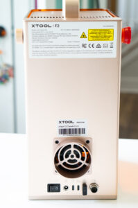 Back view of the xTool F2 laser engraver showing the cooling fan, ports, power switch, and product label.