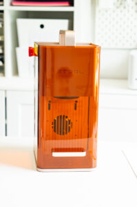 Side view of the xTool F2 portable laser engraver with its orange protective enclosure in a craft room.