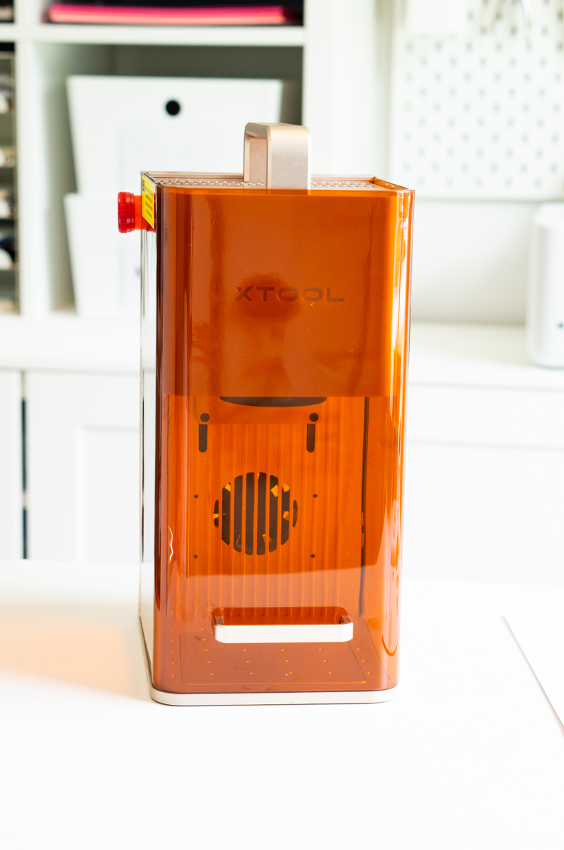 Side view of the xTool F2 portable laser engraver with its orange protective enclosure in a craft room.