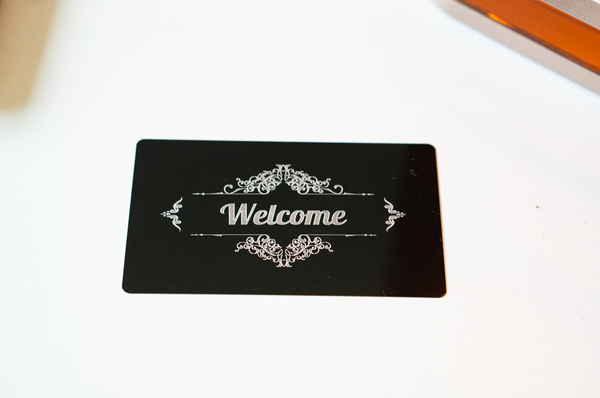 Black aluminum business card engraved with an ornate "Welcome" design using the xTool F2 laser engraver.