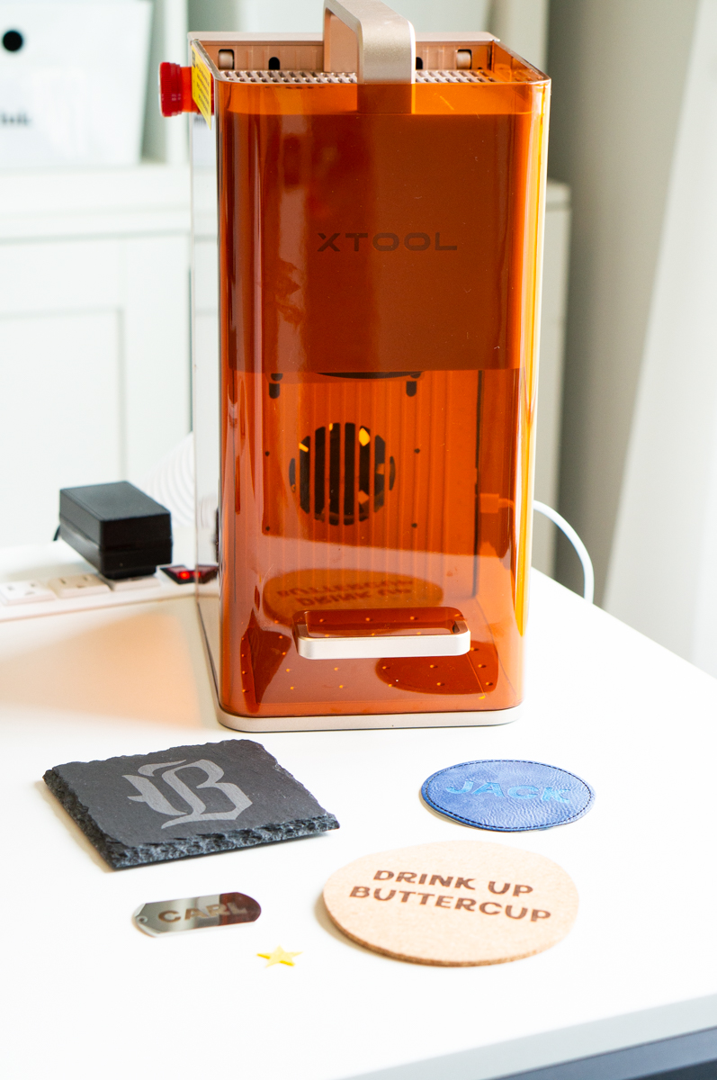 The xTool F2 laser engraver displayed with engraved sample projects including slate, leather, cork, and metal.
