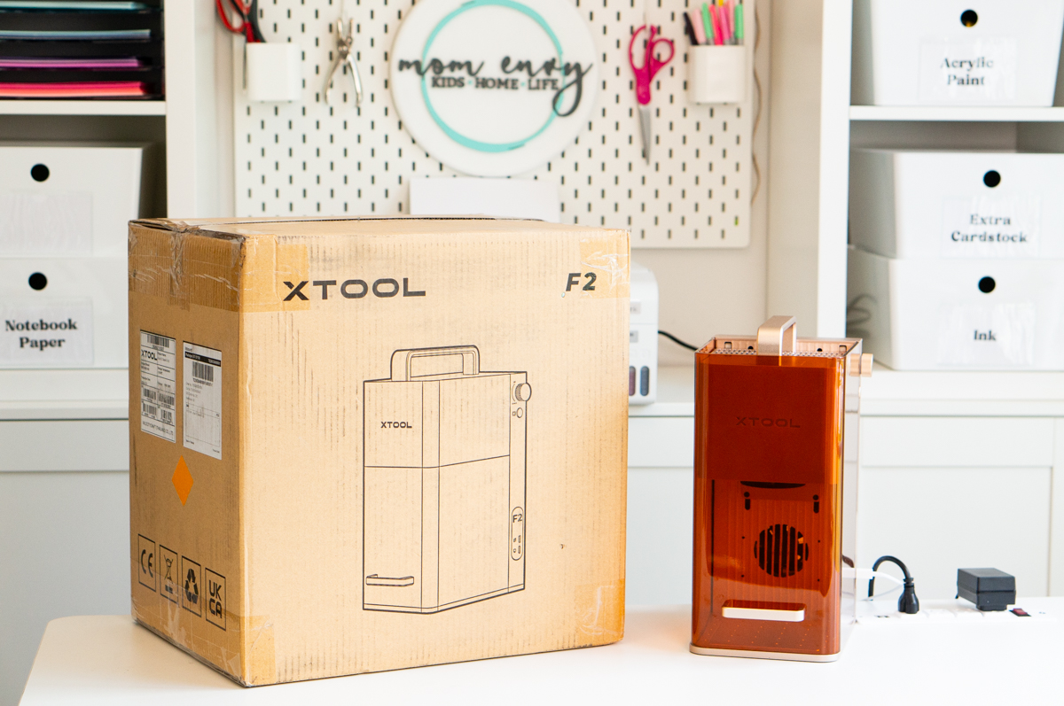 The xTool F2 shipping box displayed next to the assembled xTool F2 laser engraver in a craft room.