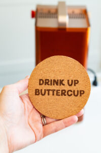 Close-up of an engraved cork coaster reading "Drink Up Buttercup" created with the xTool F2.
