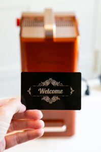 Hand holding an engraved black aluminum business card with an ornate "Welcome" design created using the xTool F2 laser engraver.
