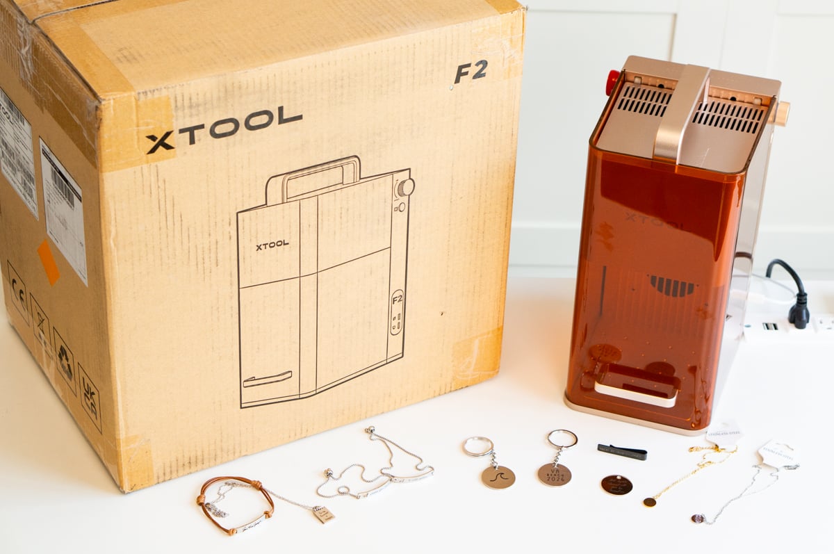 xTool F2 portable laser engraver with examples of custom engraved jewelry and keychains