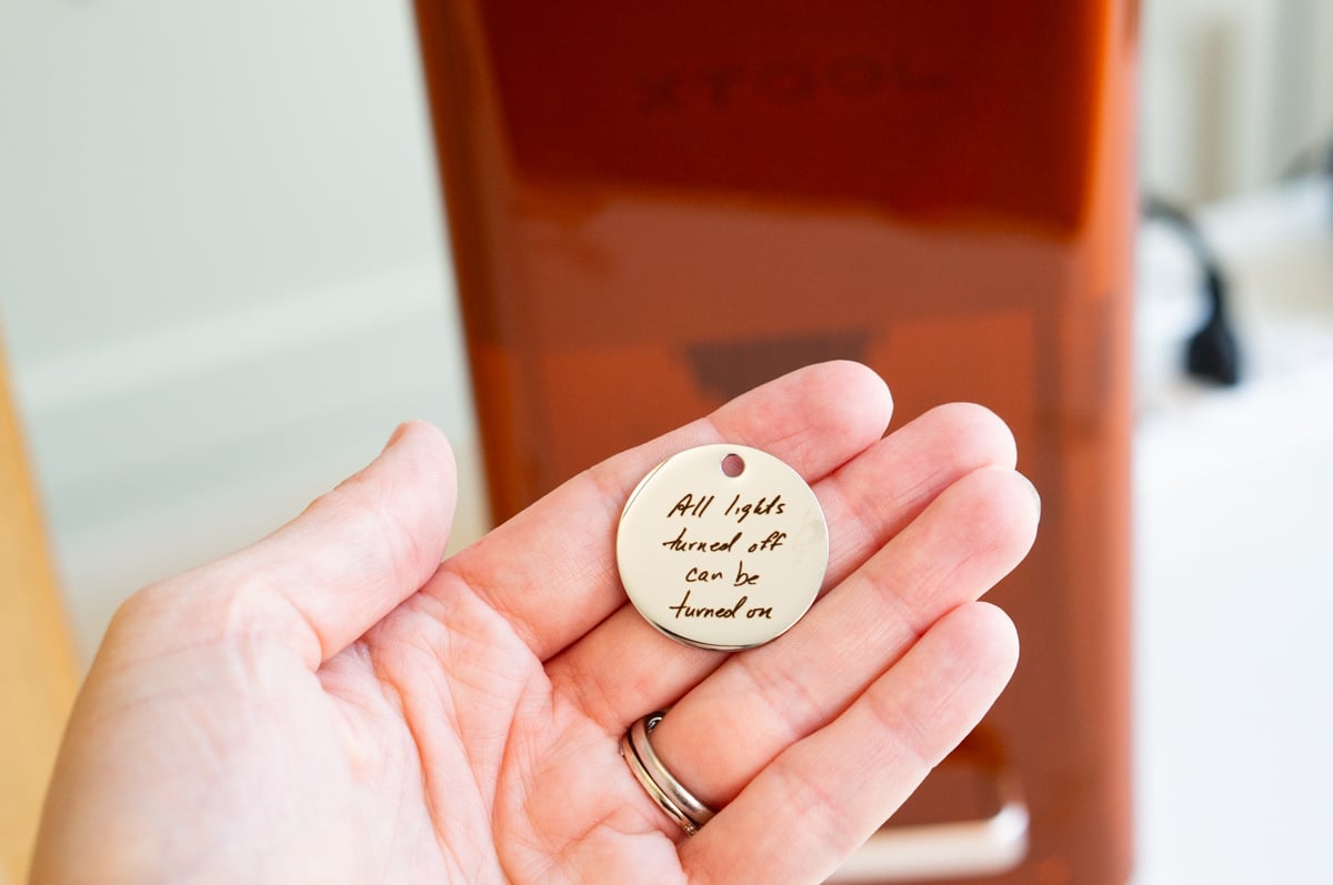 Hand holding custom metal pendant laser engraved with a handwritten message using the xTool F2