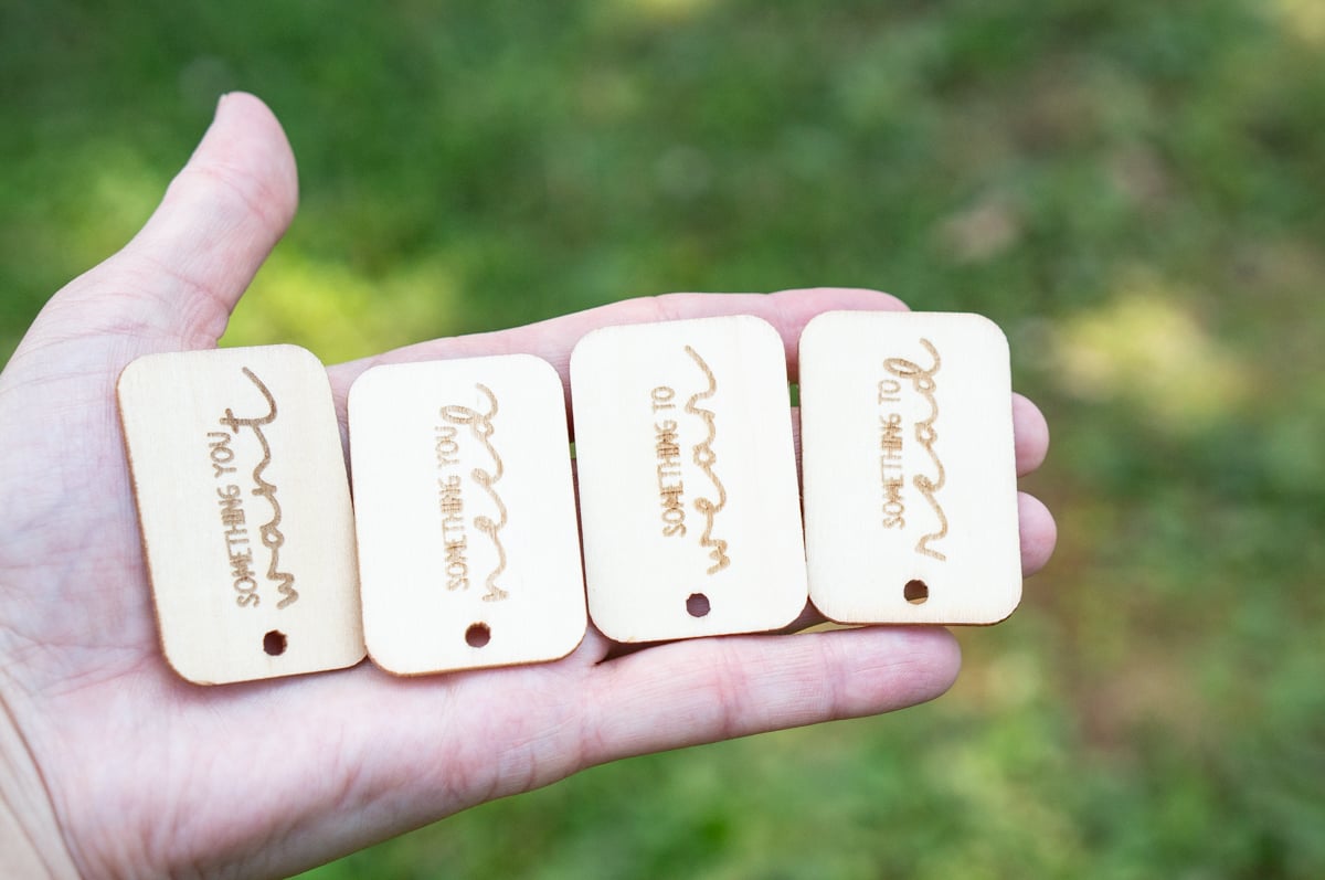 Hand holding four reusable wooden Christmas gift tags engraved with Something You Want, Something You Need, Something to Wear, and Something to Read.