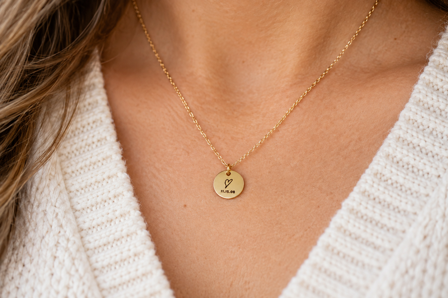 Close-up of a woman wearing a delicate gold necklace with a small round pendant engraved with a hand-drawn heart and the date 11.15.08.